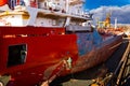 Worker paints cargo ship hull red in dry dock under blue sky. Maritime vessel maintenance, industrial painting job at Royalty Free Stock Photo