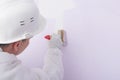 A worker paints a white wall with a brush in lilac color