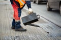 A worker pours liquid asphalt, molten bitumen from a bucket of resin.