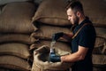 Worker pours a scoop of coffee into a device for measuring humidity from a bag, in the background of a warehouse Royalty Free Stock Photo