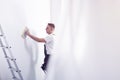 Worker priming white wall next to ladder during home renovation