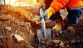 Worker in protective gear digging soil with a shovel at a construction site during sunset Royalty Free Stock Photo