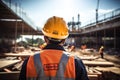 Worker with protective helmet and safety vest, rear view. Construction site background