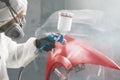 Worker in protective mask and jumpsuit overall spraying base coat of paint on car body elements in painted chamber using Royalty Free Stock Photo