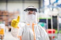 Worker with protective mask and suit in industrial factory, thumb up hand gesture.