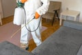 Worker in protective suit with decontamination sprayer bottle disinfecting household and furniture. Pest control concept.