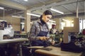 Worker punching holes in leather material of future boots in workshop of shoe factory