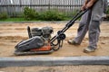 Worker rams the ground with a vibrating machine.Side view