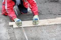 A kneeling worker manually cleans and levels the sand base with a wooden plank for future sidewalk tiling Royalty Free Stock Photo