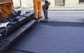 Worker regulate tracked paver laying asphalt