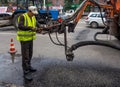 Worker repairing the hole in the asphalt on a city street using liquid asphalt supply hose through special machines