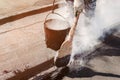 Worker repairs the roof with molten tar from a bucket with a broom