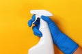 Worker`s hand in a rubber blue protective glove with a spray gun on a yellow background. The concept of cleaning, home care.