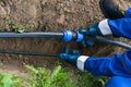 Worker`s hands hold a black pipe over a dug hole in the ground