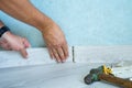 Worker`s hands Instal plastic skirting board on laminate flooring. Renovation of baseboard at home.