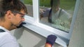 Worker in safety glasses and protective gloves installing metal sill on external PVC window frame Royalty Free Stock Photo