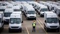 a worker in a safety vest and hard hat walking through a parking lot full of white cargo vans, a logistics or shipping Royalty Free Stock Photo