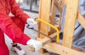 A worker is sawing wood to assemble a crate for moving an industrial machine. A woman in red mechanic coveralls hand holding a bow