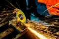 A worker saws a metal blank with a cutting wheel with a grinding machine, large sparks fly around