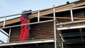 Worker on scaffolding installing new wooden planks on house roof eaves