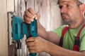 Worker scraping vertical wooden surface with vibrating sander -