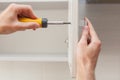 The worker sets a new handle on the white cabinet with a screwdriver.