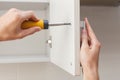 The worker sets a new handle on the white cabinet with a screwdriver.