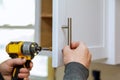 The worker sets a new handle on the white cabinet with a screwdriver Royalty Free Stock Photo