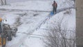 A worker with a shovel and a tractor with a bucket shovel snow in a heavy snowfall on a winter day.Natural anomalies snow is plent