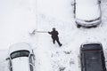 Worker shoveling snow after snowfall on road, parking near car