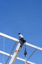 A worker sitting on the extended boom of a crane