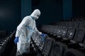 Worker in special suit wiping chairs rag in cinema hall.