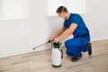 Worker Spraying Pesticide On Wall At Home