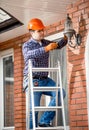 Worker standing on high ladder and changing bulb at outdoor lamp