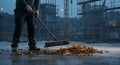 Worker sweeping autumn leaves at construction site in evening Royalty Free Stock Photo