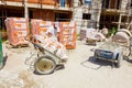 Worker is taking off hook of crane from wheelbarrow full of waste, plastic foil, works on building site