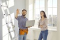 Happy worker with laptop talking to young woman about repairs and renovations in her house Royalty Free Stock Photo