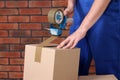 Worker taping box with adhesive tape dispenser near brick wall, closeup