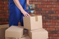 Worker taping box with adhesive tape dispenser near brick wall, closeup