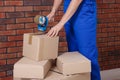 Worker taping box with adhesive tape dispenser near brick wall, closeup Royalty Free Stock Photo