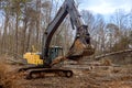 Worker to uproot trees in a forest, using an excavator to prepare ground for construction of house.