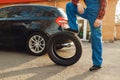 Worker in uniform poses with tyre, tire service