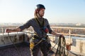 A worker unwinds a climbing rope on the roof of a high-rise building. Sunny weather, cheerful photo of an industrial climber in Royalty Free Stock Photo