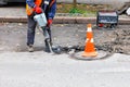 A worker uses an electric jackhammer to loosen old asphalt as he repairs a fenced road section