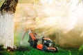 Worker using industrial lawnmower against direct sunlight, details of landscaping and gardening