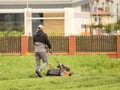 Worker using a manual lawn mower mows grass on near the house. Landscaping and maintenance of green spaces of the
