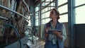 Worker walk milking parlour at dairy facility. Woman inspect suction machinery.