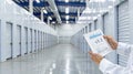 A worker in a warehouse stands in an aisle and looks at a tablet that displays a data chart Royalty Free Stock Photo