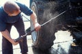 Worker washes under pressure bottom of wheeled tractor with water gun. Heavy equipment car wash