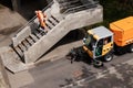 Worker wearing orange uniform cleaning city stairs with leaf blower and a street sweepers vehicle cleaning the sidewalk